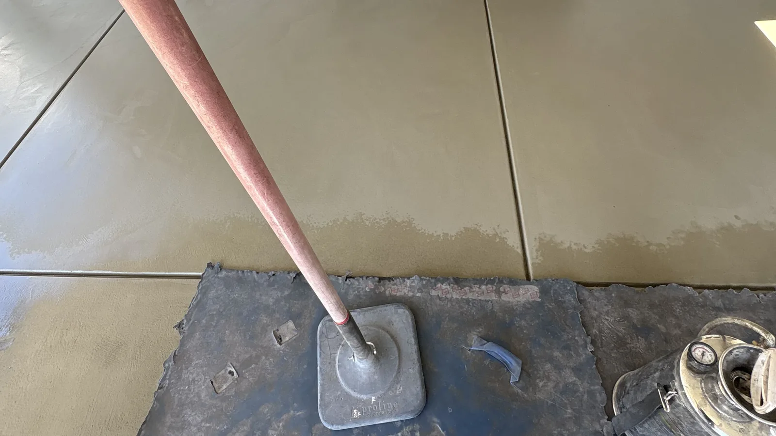 Long-handled float resting on a fresh concrete pour being finished beside a house wall