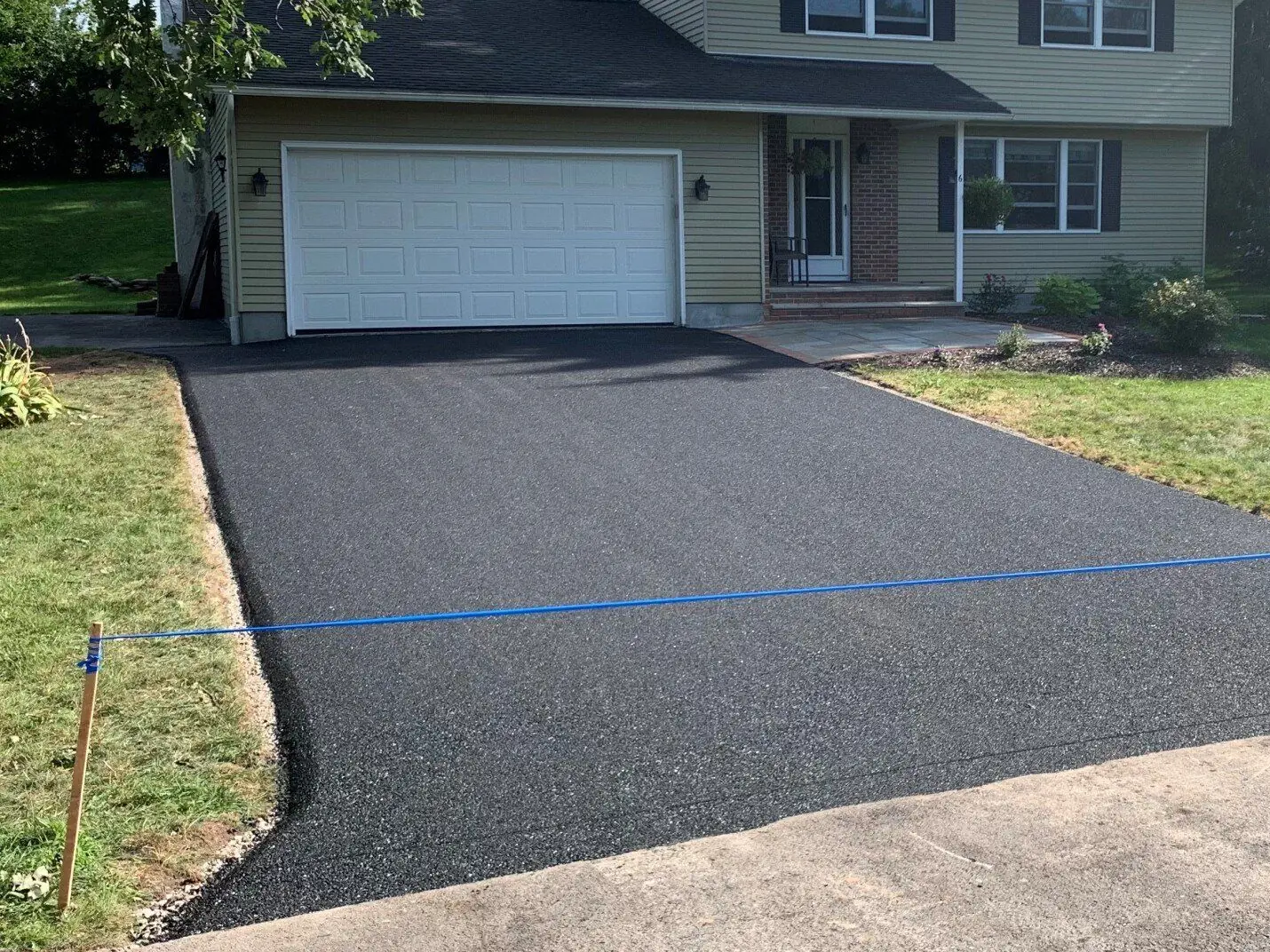 A newly paved asphalt driveway running up to a two car garage, roped off with a string line while it cures