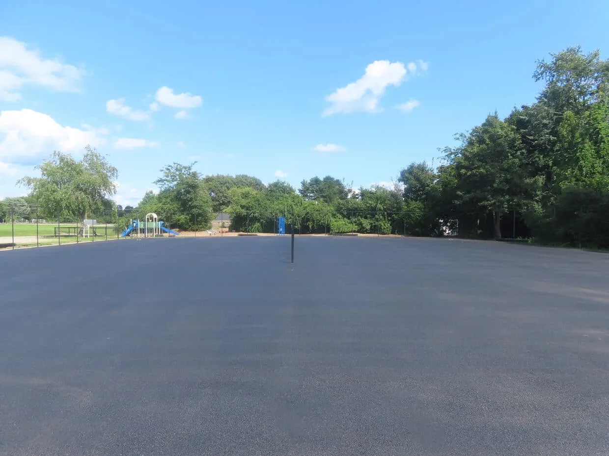 A freshly paved asphalt parking lot with trees along the far edge
