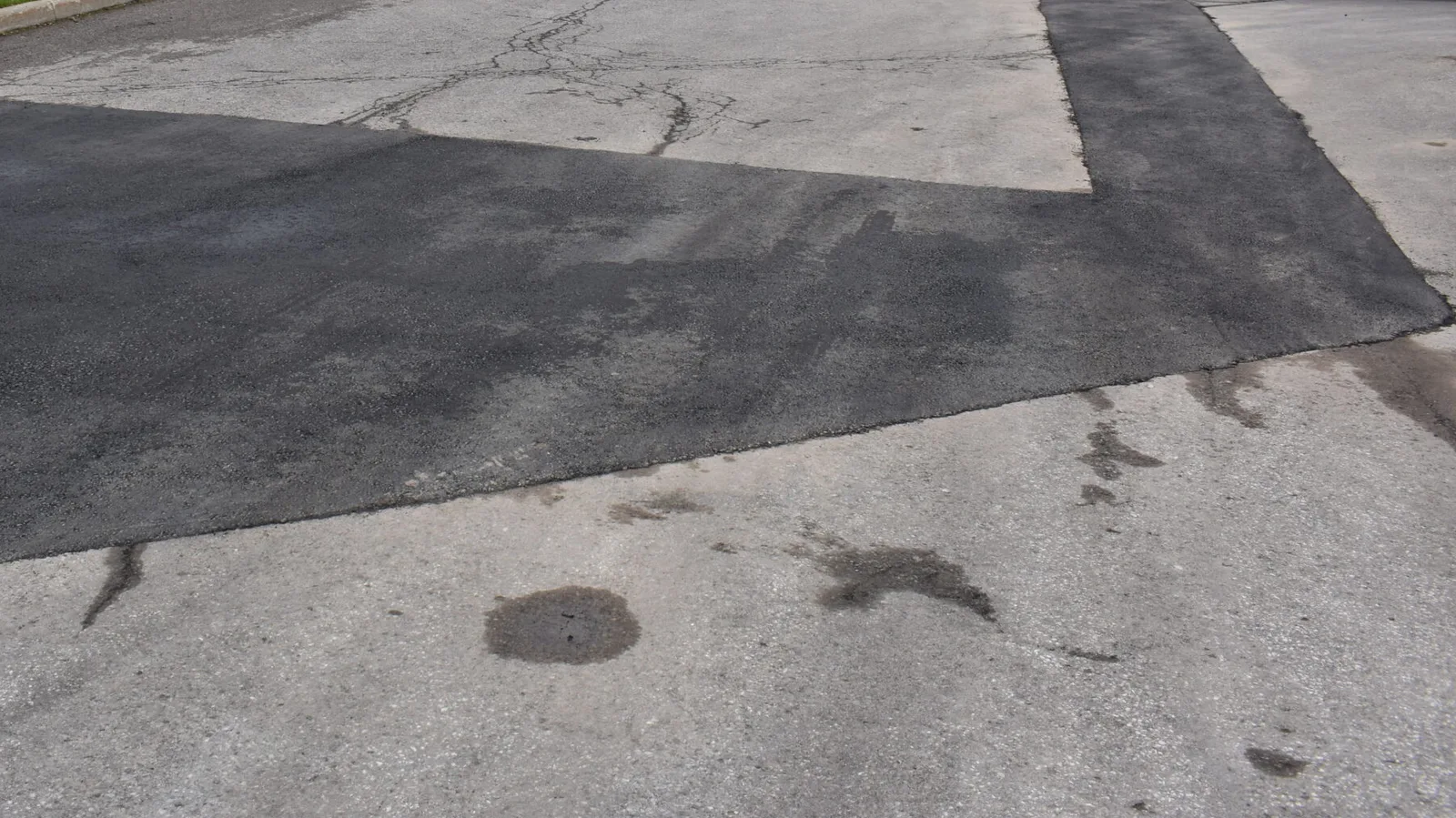 A saw cut asphalt patch in a parking area, the new hot mix darker than the older pavement around it