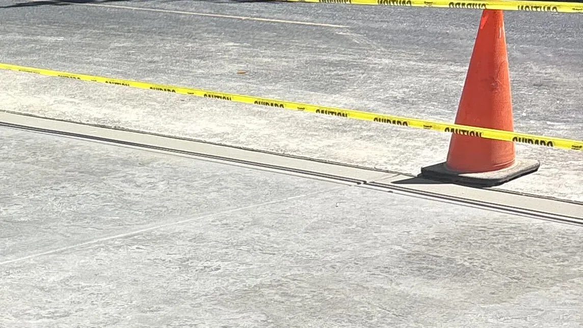 New concrete driveway pad meeting an asphalt street, taped off with caution tape and a cone while it cures