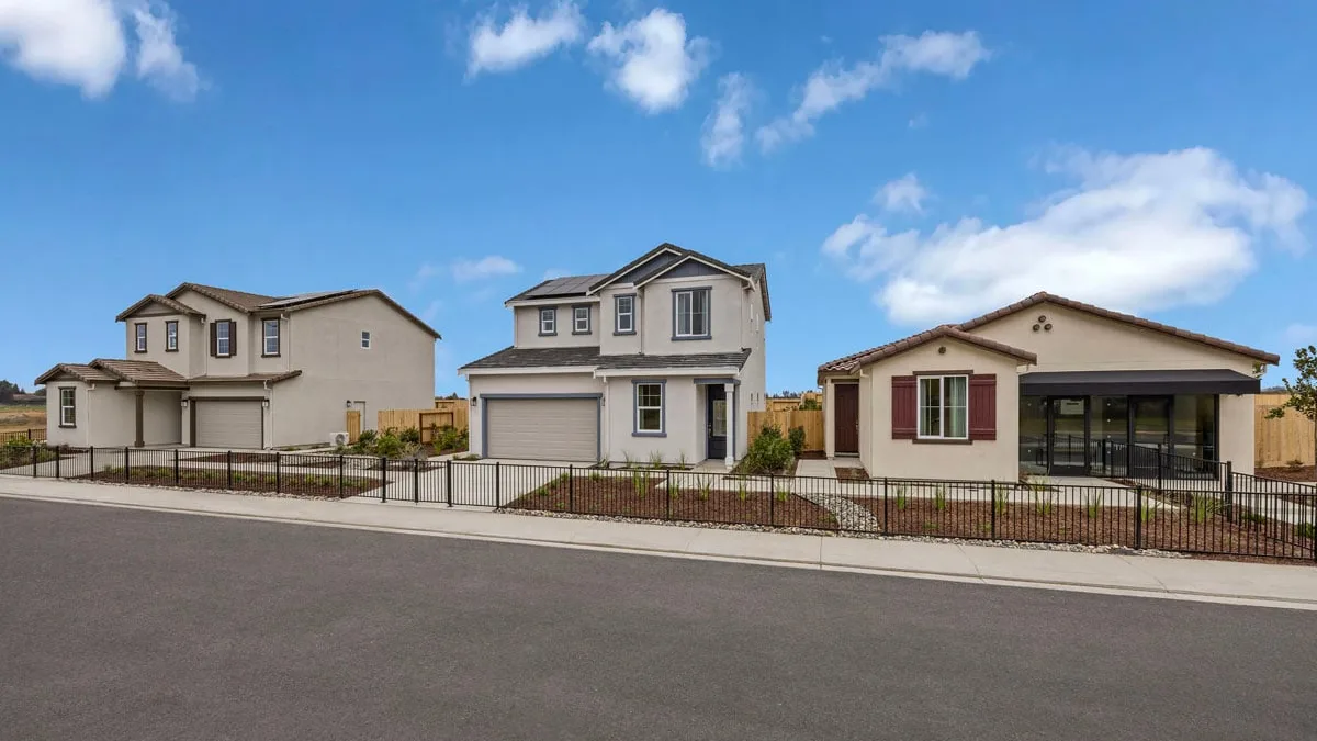 Row of newly built stucco homes with tile roofs along a residential street with a concrete sidewalk and curb