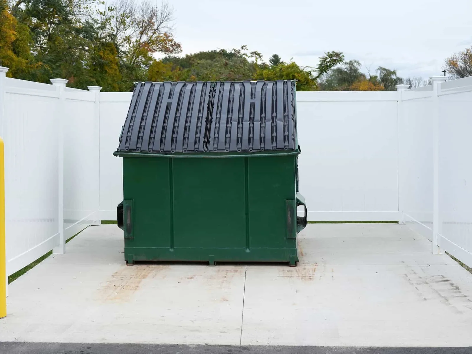Concrete dumpster pad inside a fenced commercial enclosure