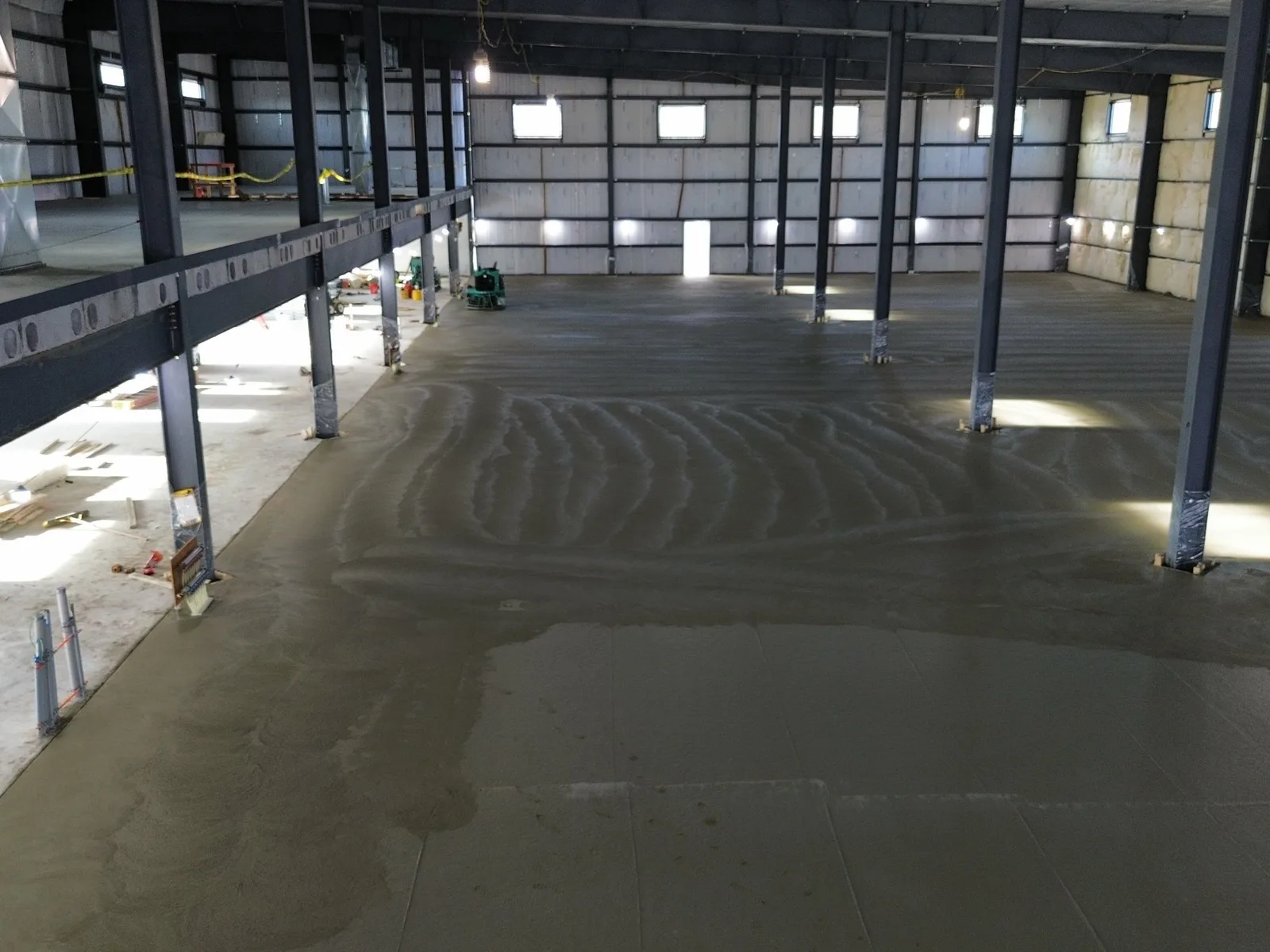 Large freshly poured commercial concrete floor slab inside a steel-framed building
