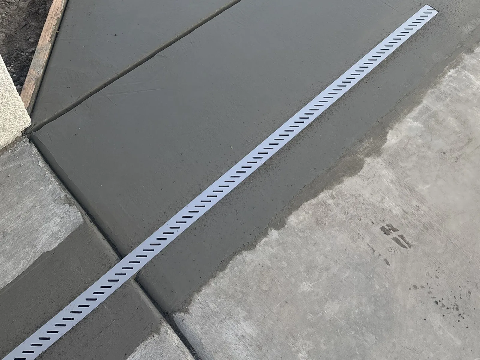 Close view of a poured concrete walkway with a linear channel drain and sawcut joints beside a planted border