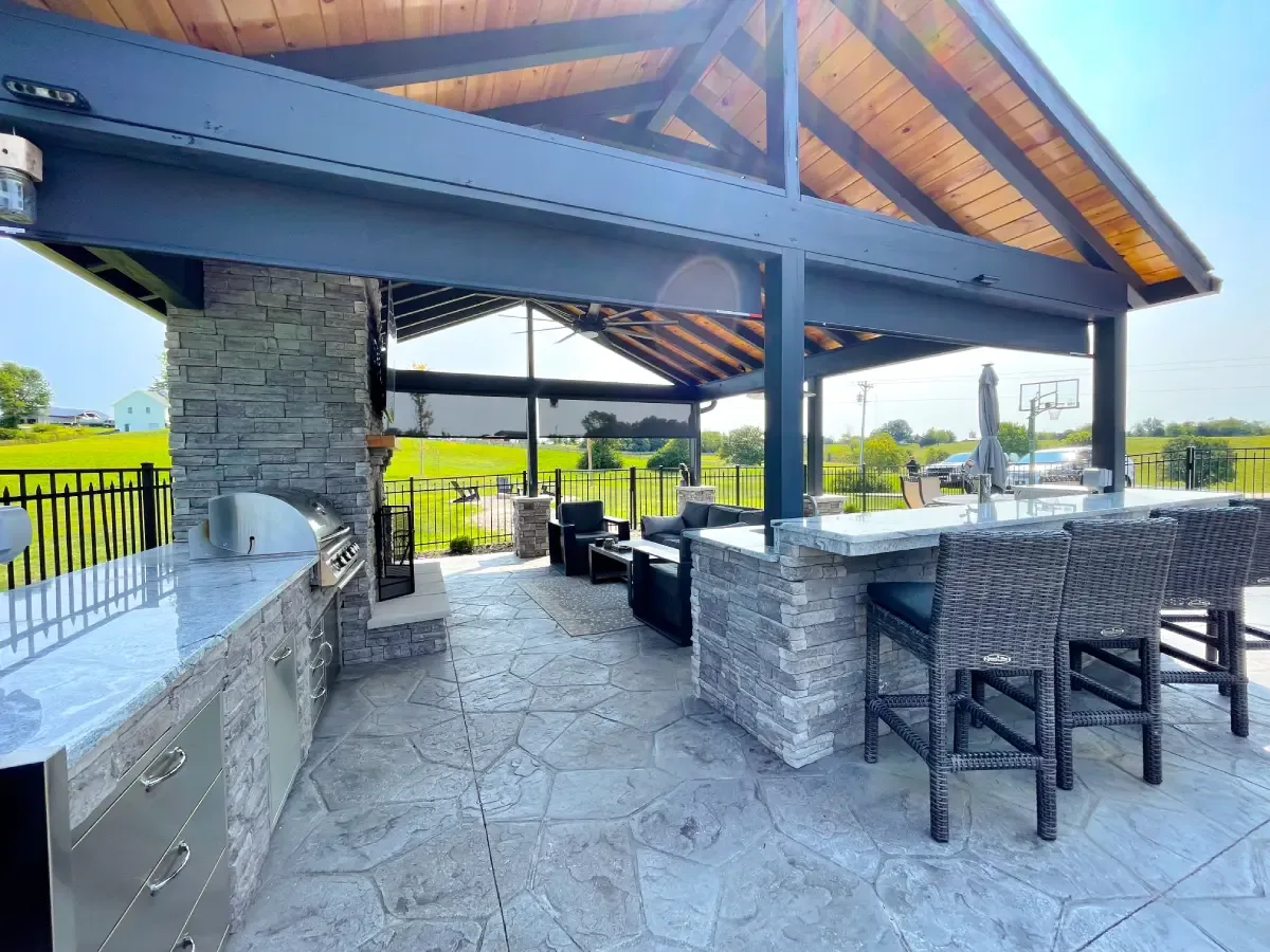 Stamped concrete floor under a covered outdoor kitchen and bar with a grill and seating