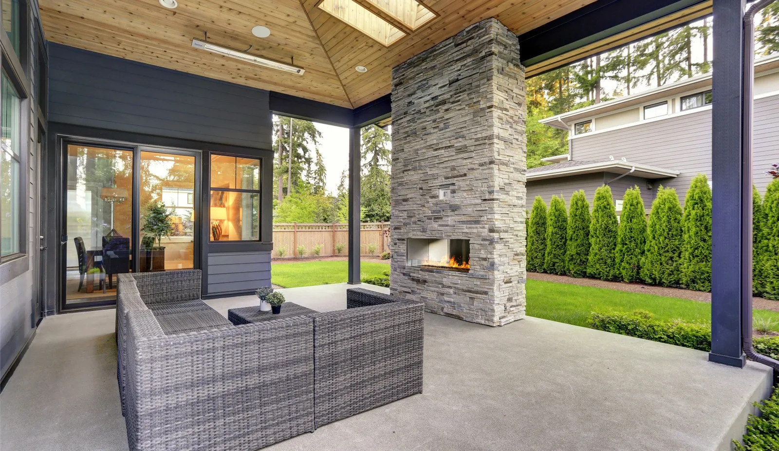 Plain concrete floor under a covered back patio with a stone fireplace at a newer home