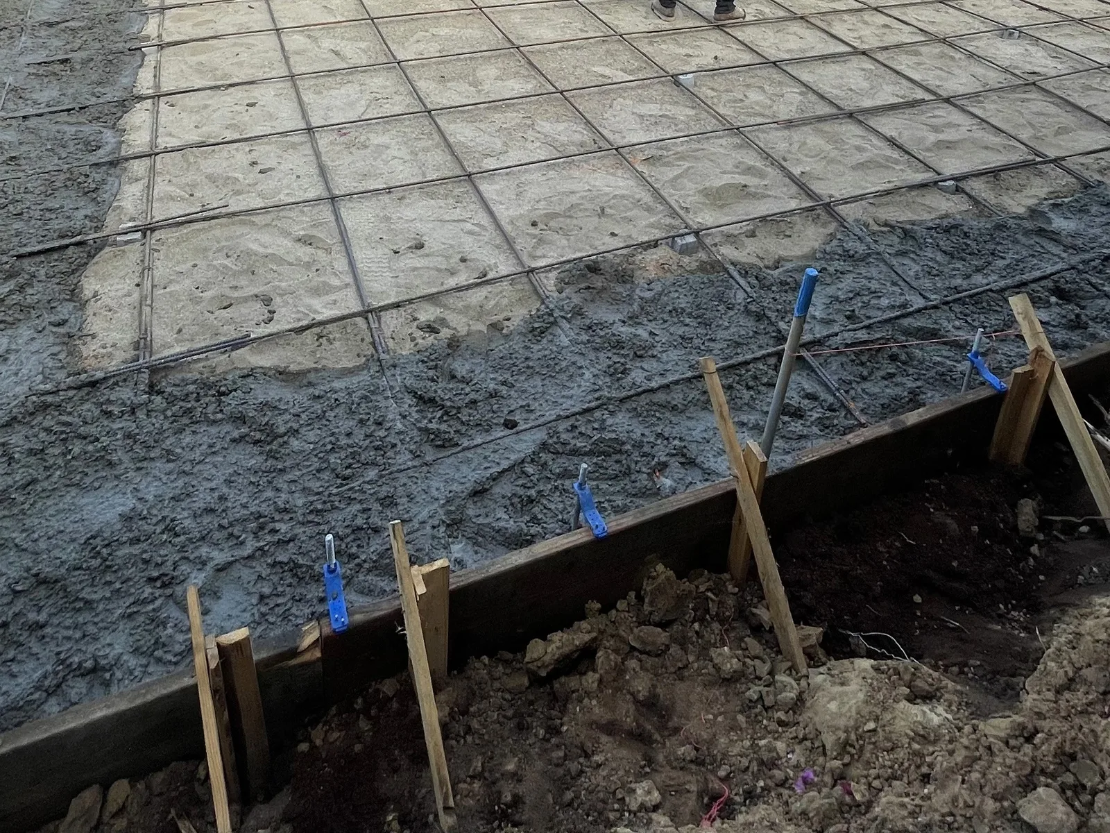 Wire mesh laid over a prepped slab foundation inside wood forms, ready for a concrete pour