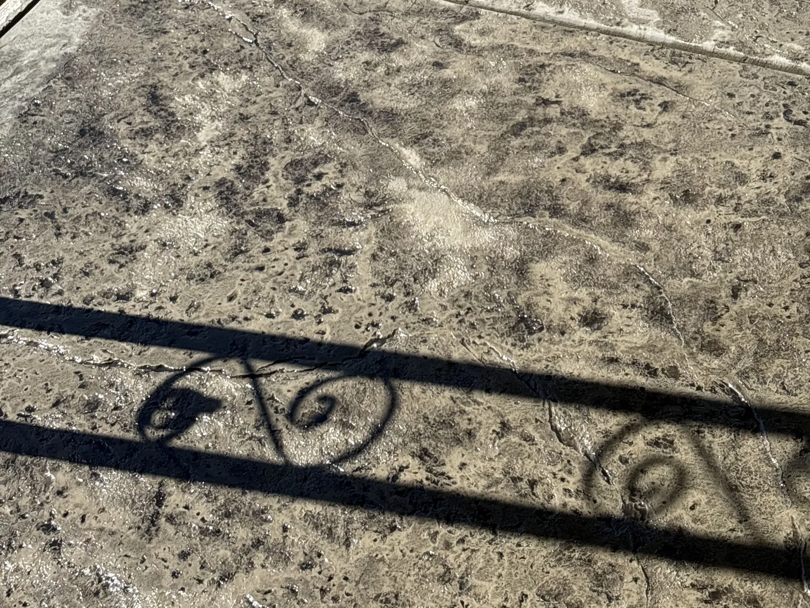 Stamped concrete patio surface with the shadow of a wrought-iron railing falling across it