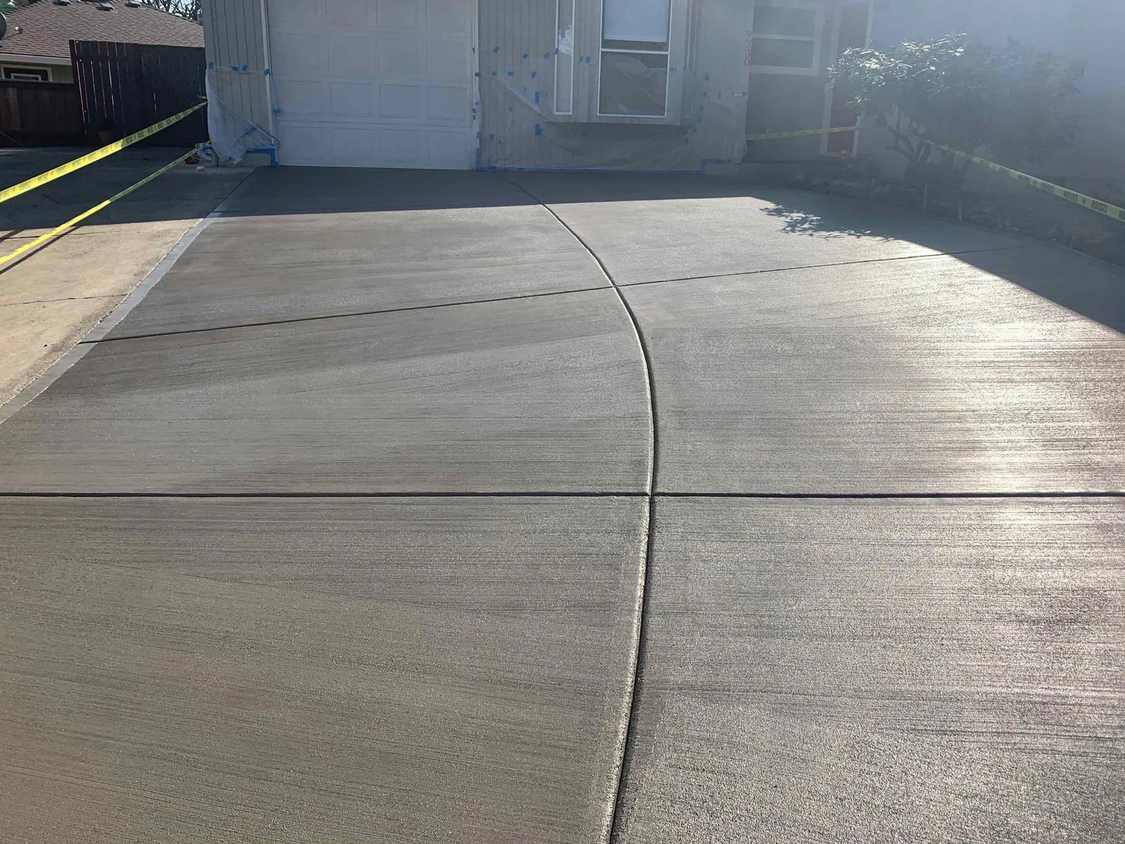 Newly poured broom-finish concrete driveway with a curved control joint in front of a single-story home
