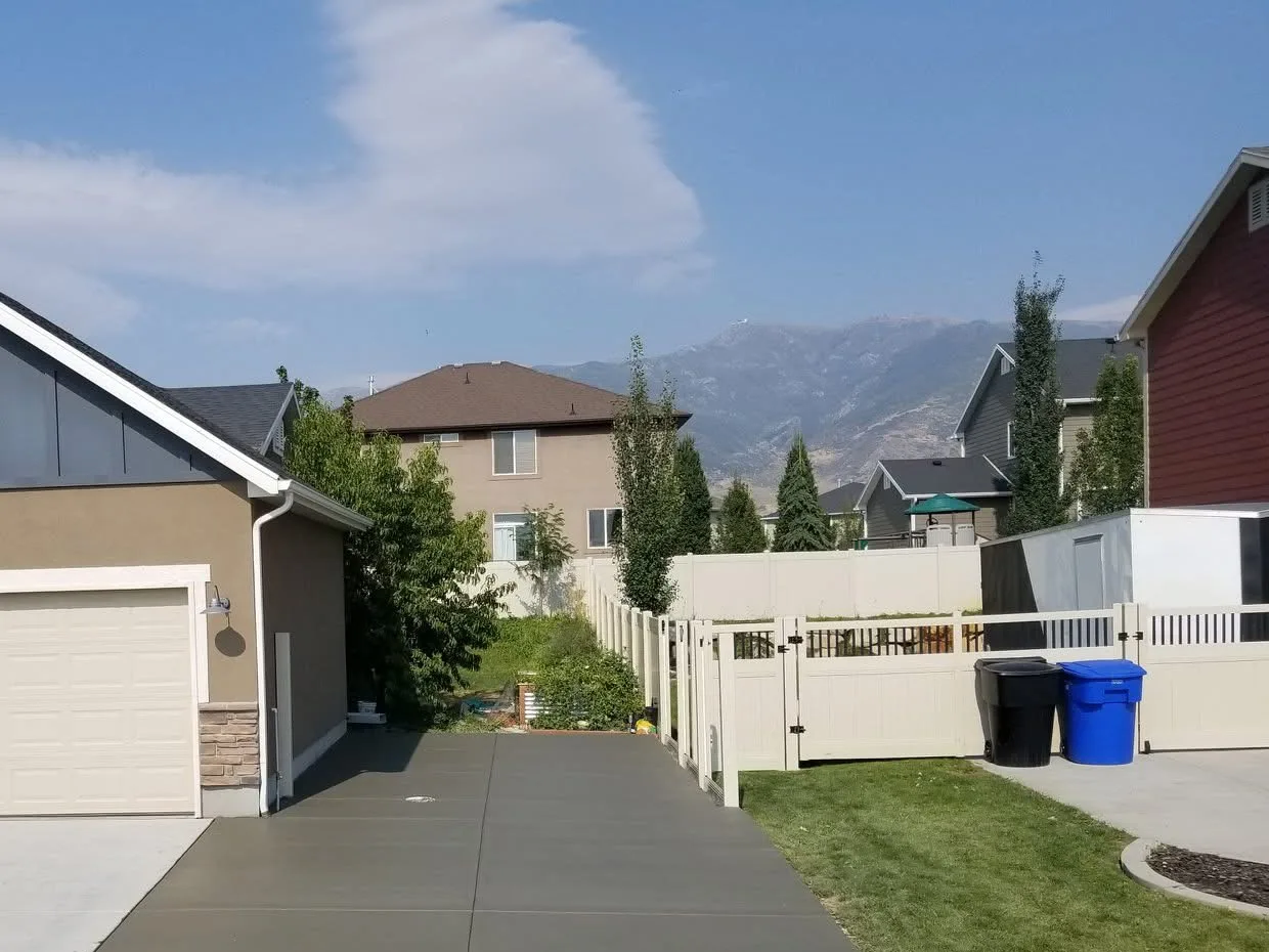 Wide concrete driveway extension and parking pad running alongside a garage to a side gate