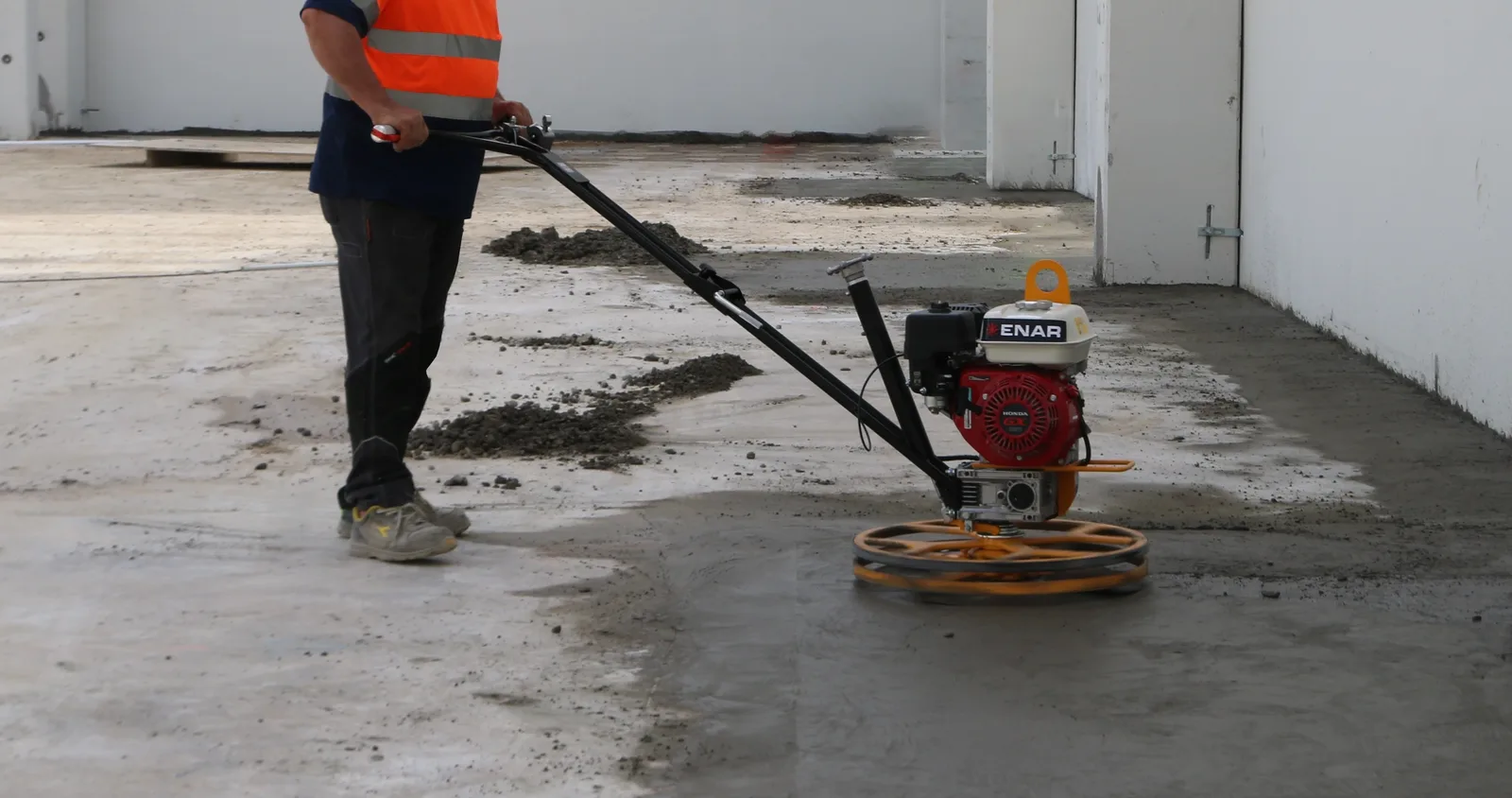 Concrete finisher running a walk-behind power trowel across a freshly poured slab