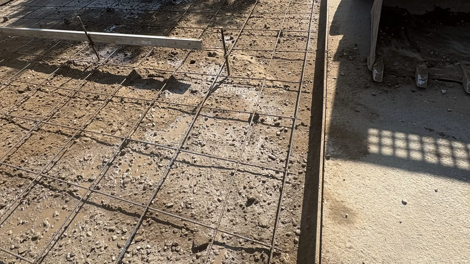 Rebar grid tied over a compacted gravel base on a prepped driveway pad, with a skid steer at the edge of the pour