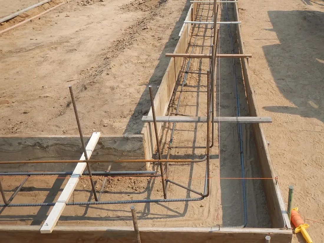 Formed footing trench with tied rebar and conduit ready for a foundation pour