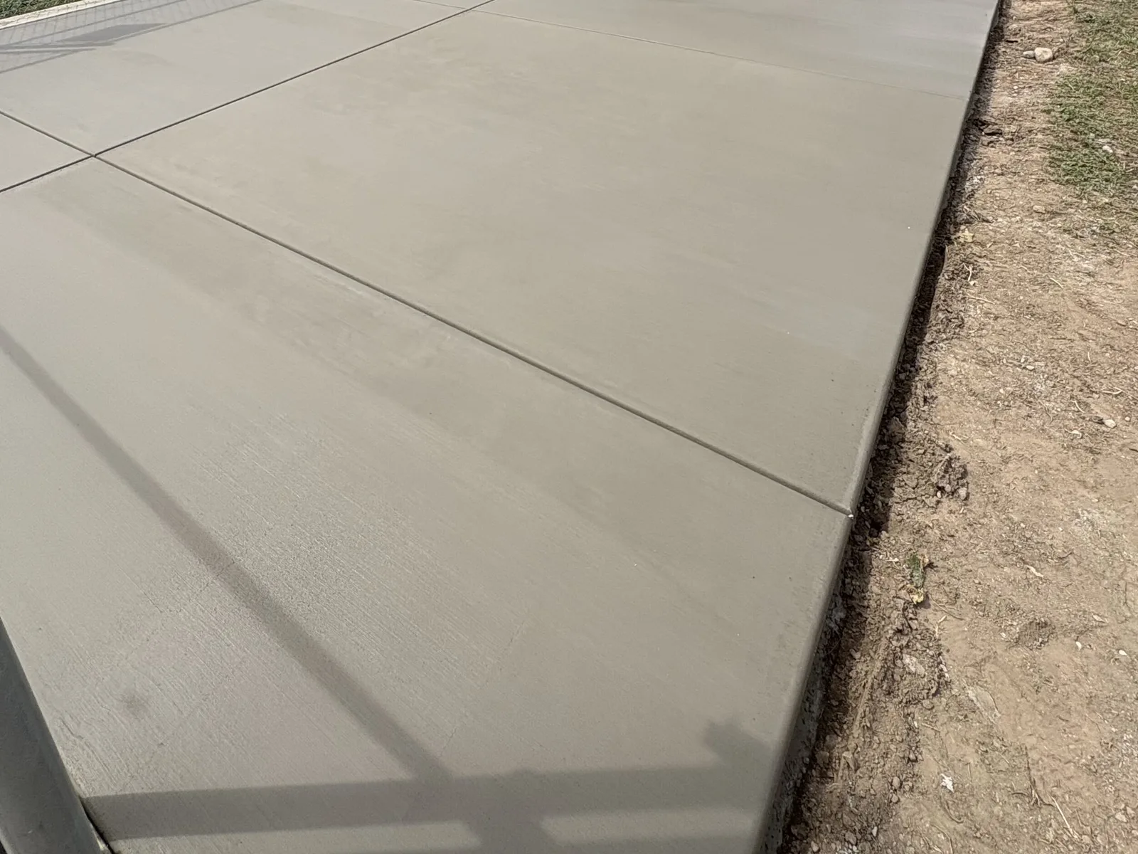 Finished broom-finish concrete walkway running along a chain-link fence beside an open field