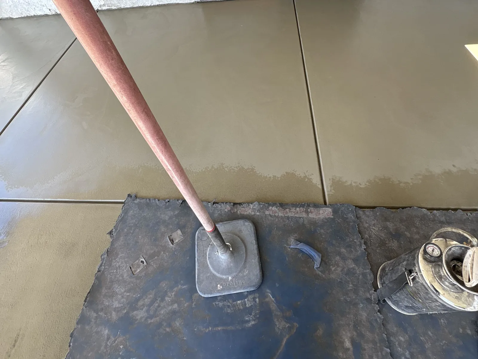 Fresh concrete slab being finished beside a doorway, with a long-handled float resting on the wet surface