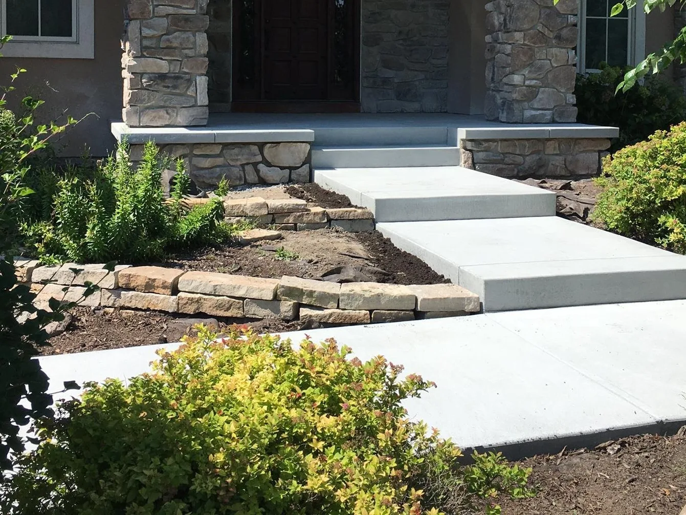 Poured concrete steps and landing leading up to a front entry, with a concrete walkway below