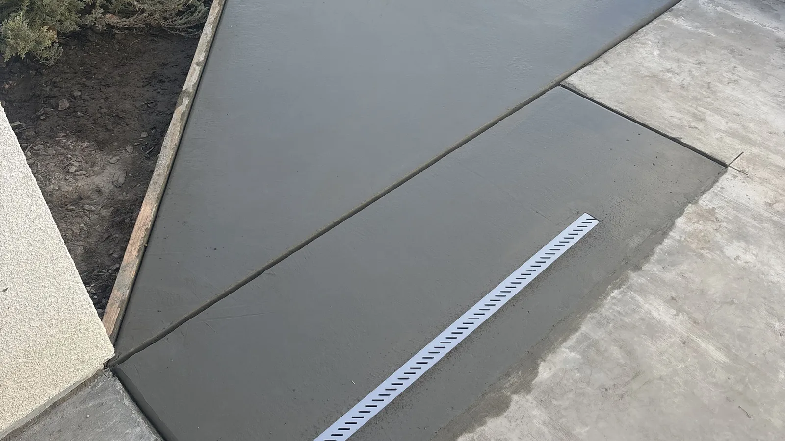 Freshly poured concrete side-yard walkway with a linear channel drain set into it and sawcut control joints