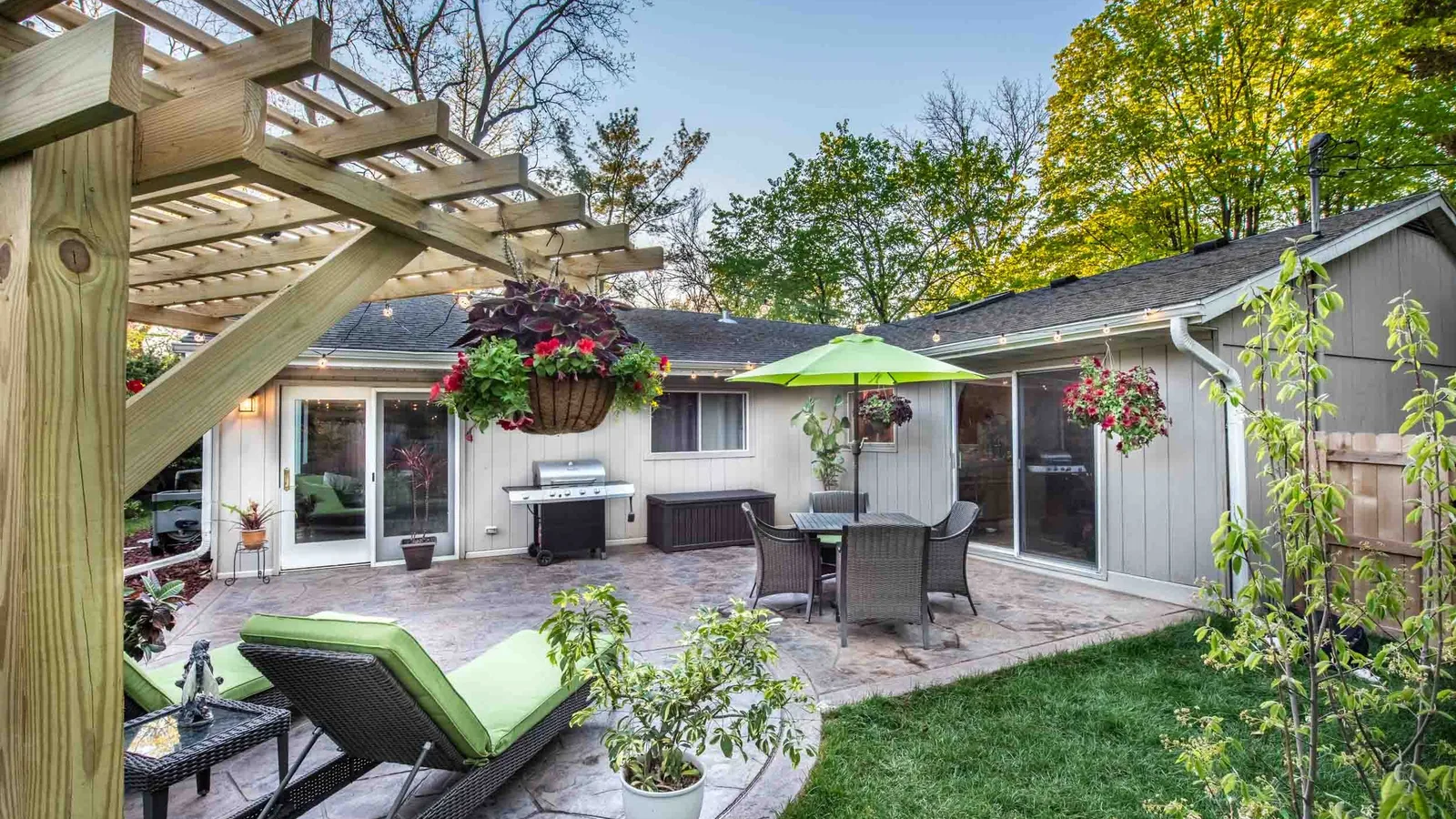 Finished stamped concrete patio with a pergola, dining set and grill in a backyard at dusk