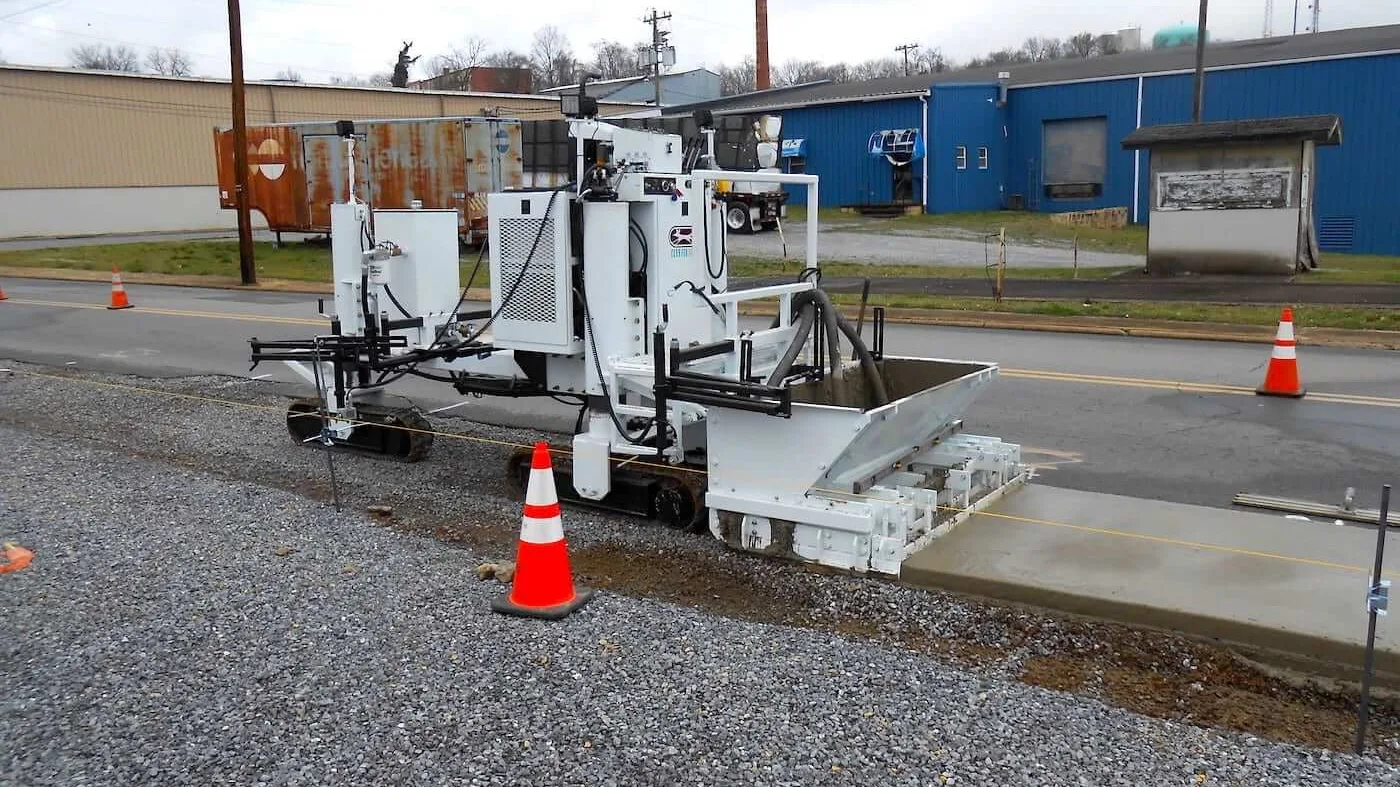 Slipform curb machine extruding a concrete curb and gutter along a street edge