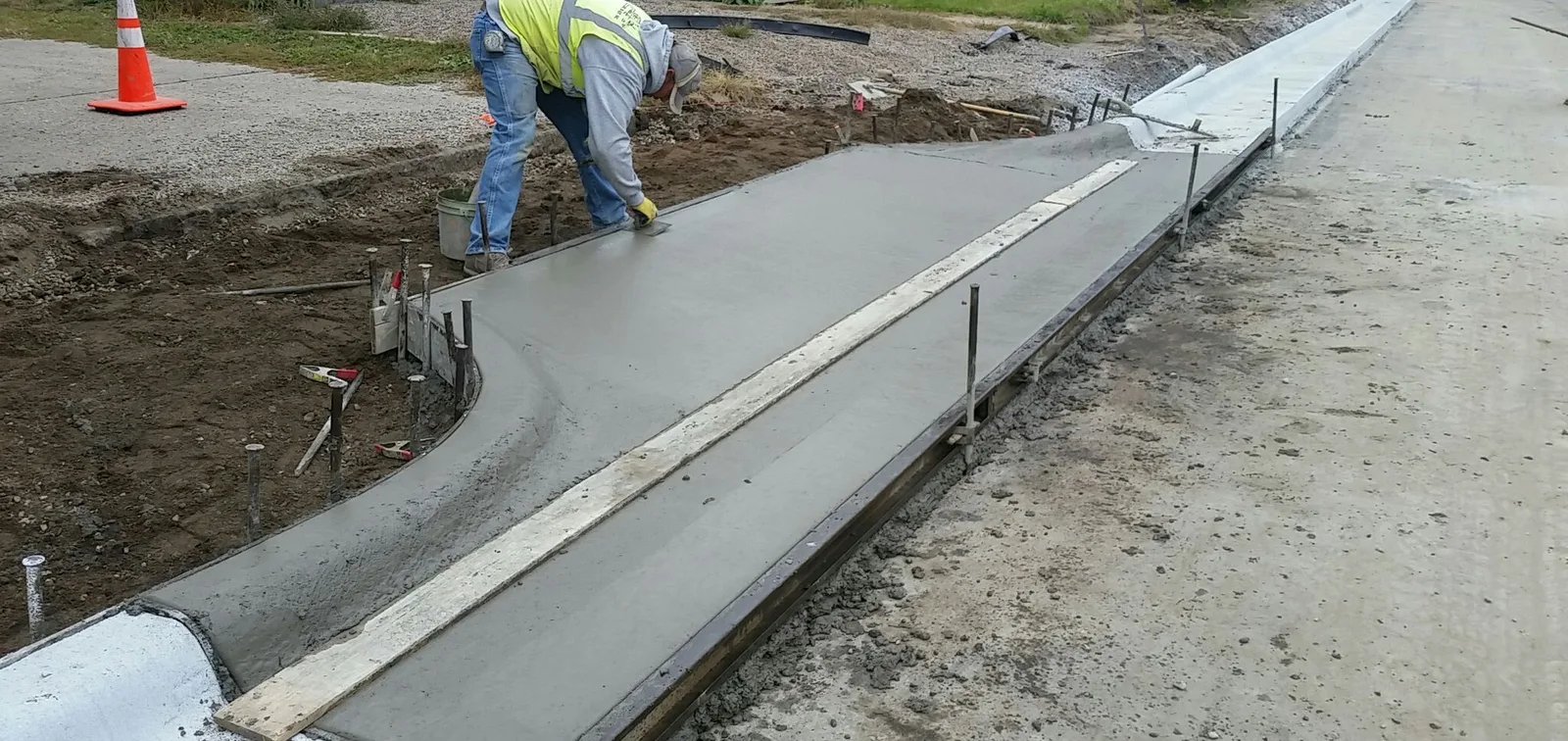 A finisher working a freshly poured driveway approach along the curb line