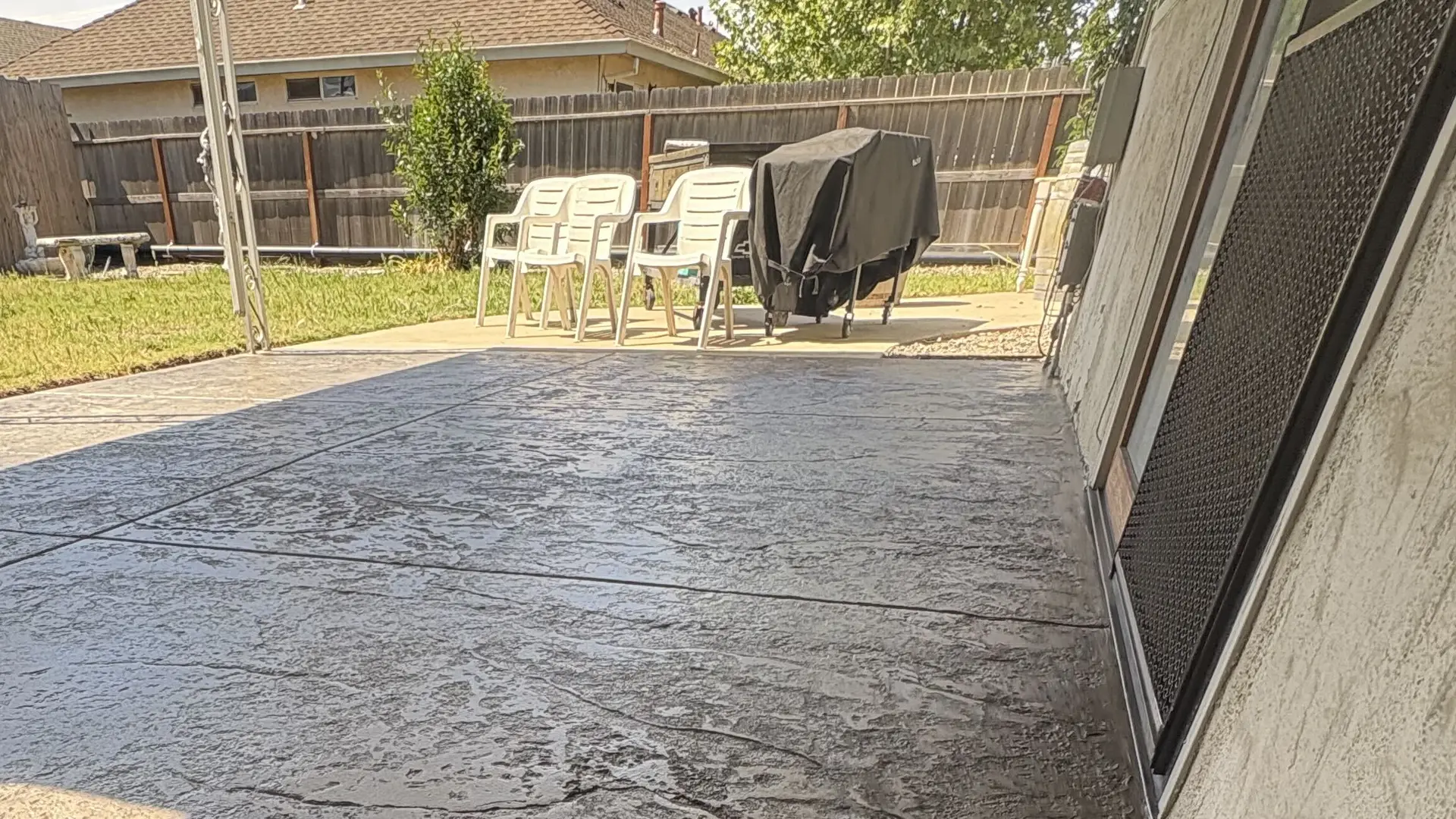 Stamped concrete patio under a covered porch looking out to a fenced backyard with patio chairs and a barbecue at a Modesto-area home