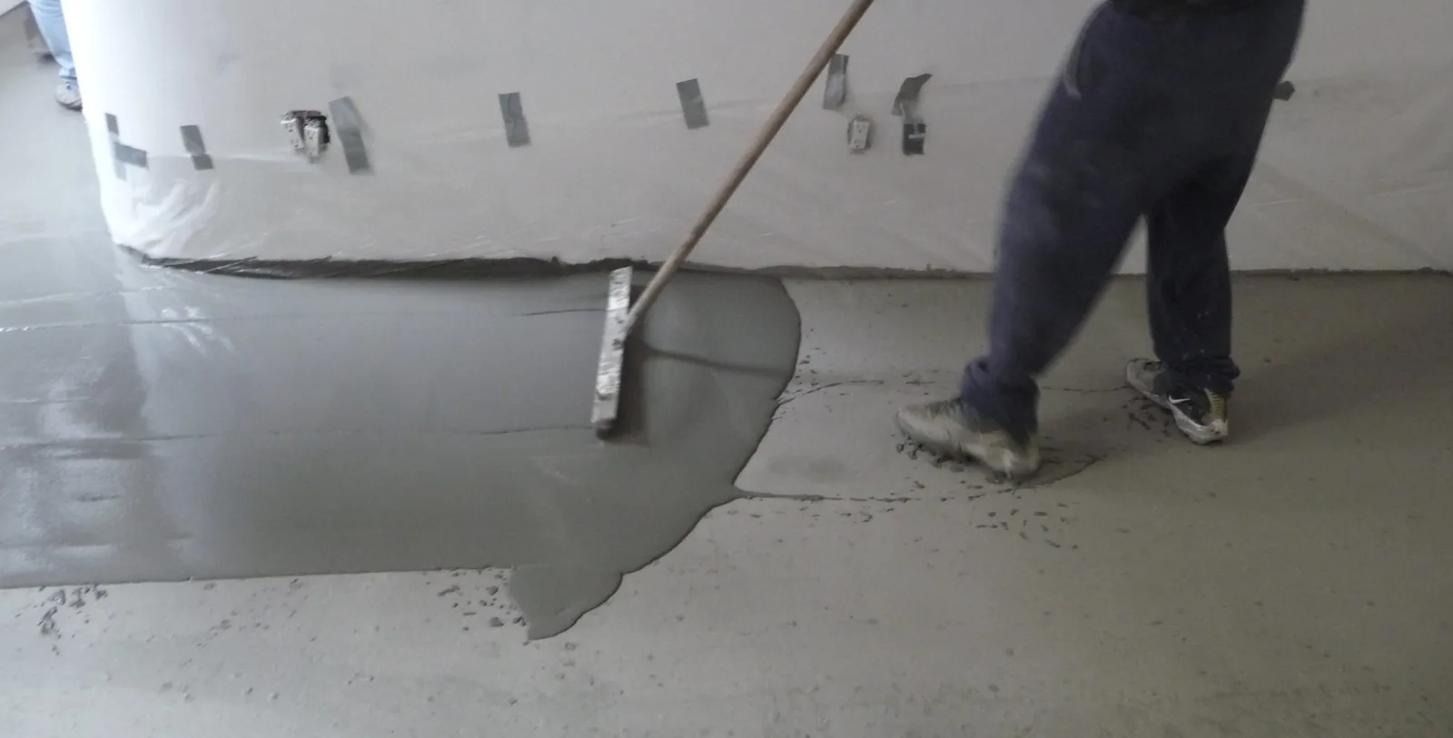 Worker spreading a thin micro-topping overlay across a concrete floor with a gauge rake