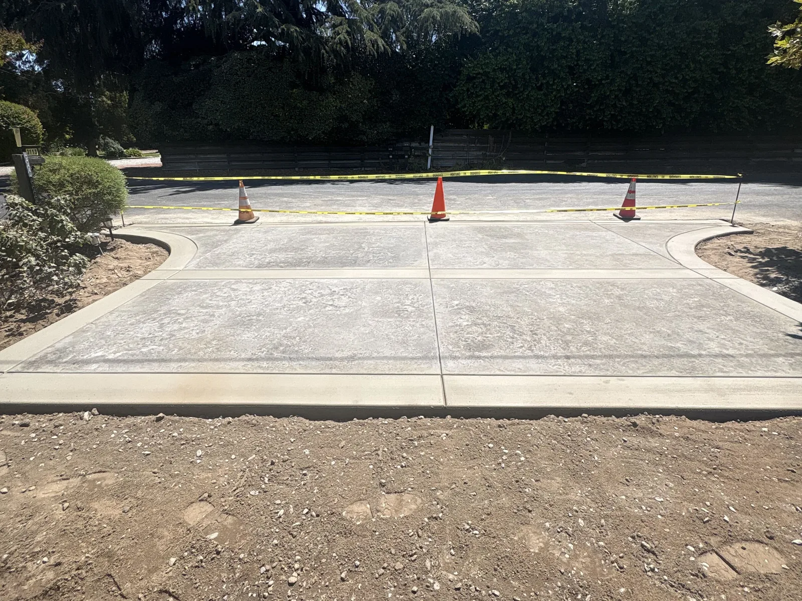 Newly finished concrete driveway seen from the street, roped off with caution tape and traffic cones under trees