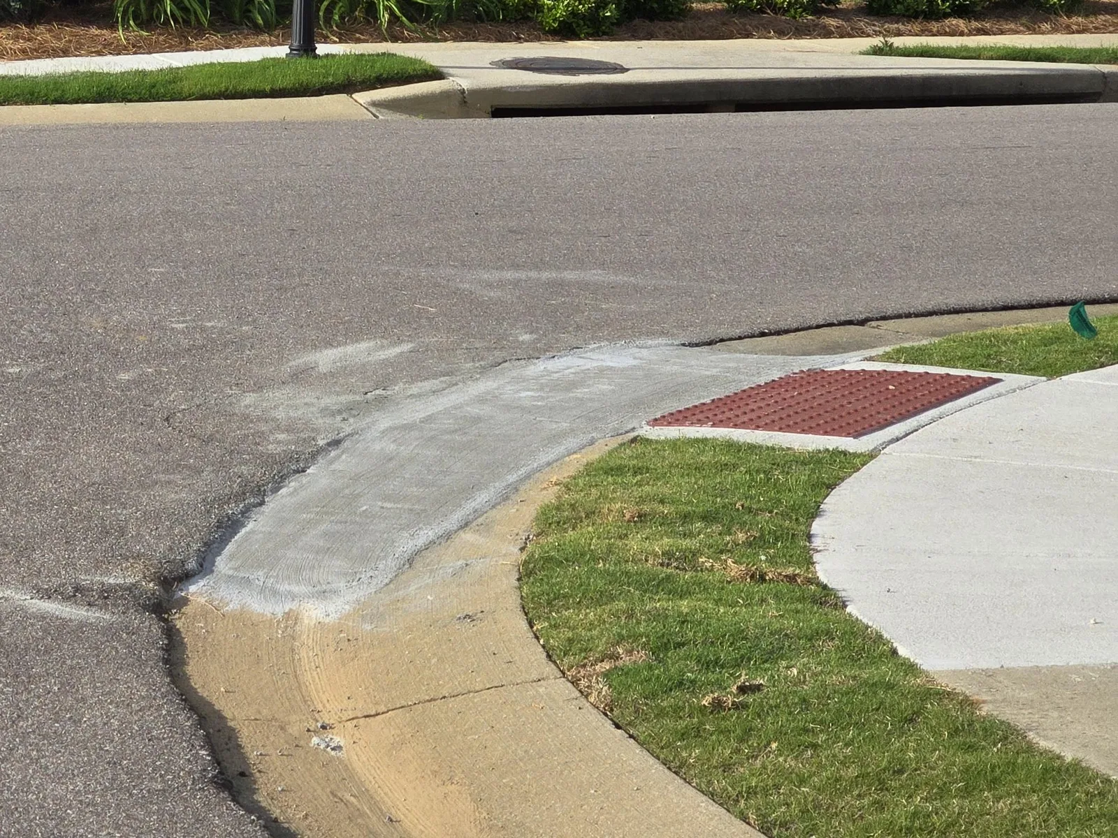 Rolled concrete curb and gutter sweeping around a residential corner beside a sidewalk ramp