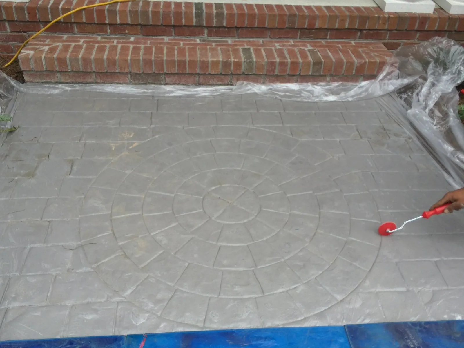 Stamped concrete overlay with a circular pattern being sealed with a roller over an existing stoop